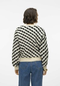 Mönstrad tröja med en krämfärgad bas och svarta vågiga ränder, ribbade mudd och nederkant. Matchas med högmidjade blå denimjeans.