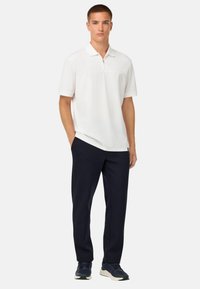 Bílá polo tričko s krátkým rukávem a předním zipem, kombinované s námořnickými kalhotami a tmavou obuví. Hladká látka, jednoduchý design.