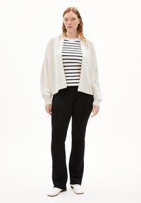 White knit cardigan over a black and white striped shirt, paired with black pants and white shoes. Simple, relaxed fit, and clean lines.