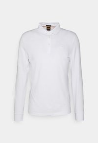 Vit långärmad polo skjorta i bomull. Har en knappslå, ribbade manschetter och en liten logotyp på bröstet.