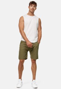 Chemise sans manches gris clair et short vert olive avec un motif texturé. Le modèle porte des baskets blanches et se tient les mains dans les poches.
