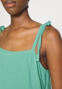 En ärmlös, mintgrön klänning med knutna axelband, som har en avslappnad passform och mjukt, texturerat tyg. Noterbar sidoficka.