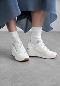 Weiße Sneakers mit strukturiertem Design, bestehend aus einer Mischung aus glatten und Netzmaterialien, Schnürsenkeln, seitlichen Reißverschlüssen und einer leichten Gummisohle.