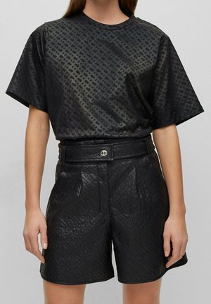 Femme portant un haut noir à manches courtes avec motif et un short ceinturé taille haute assorti avec un design géométrique texturé.