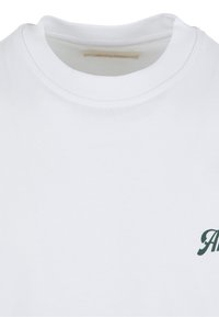Weißes T-Shirt mit Rundhalsausschnitt und teilweise grüner kursiver Schrift im unteren rechten Bereich sowie sichtbarem Innenetikett am Kragen.