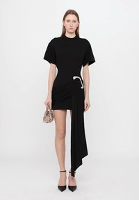 Musthave musta lühike kleit, millel on liibuv rinnaosa, ülepaisutatud varrukad ja voogav küljeosa. Kombineeritud väikese mustriga kotiga ja kontsadega.