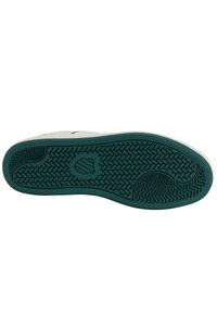 Gummisula med ett mönster som har en central logotyp; släta kanter; dominerande mörkgrön färg med en vit övre kant.