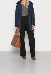 Abrigo acolchado azul marino con cremallera, blusa floral, pantalones de pierna ancha negros, bolso de cuero marrón y zapatos de tacón marrón.