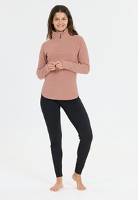 Leichtes Langarmoberteil aus weichem Rosenstoff mit einem halben Reißverschlusskragen. Kombiniert mit schwarzen, eng anliegenden Leggings. Glatte Textur, minimalistisches Design.