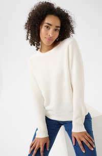 Pull en tricot couleur crème avec des manches longues et des poignets côtelés. Texture douce avec un col rond classique, associé à un jean en denim bleu.