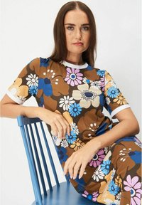 Kukallinen mekko ruskeasta, sinisestä ja vaaleanpunaisesta kankaasta. Sillä on pyöreä pääntie ja valkoiset hihansuut. Sujuva rakenne ja rento istuvuus.