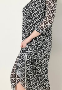 Robe à motifs noir et blanc avec des manches trois-quarts, ornée de designs géométriques. Fabriquée en tissu léger avec une silhouette fluide.