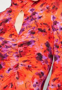 Robe à motif floral avec une base orange vive et des accents violets, col haut, détail en trou de serrure et texture froncée à l'avant.