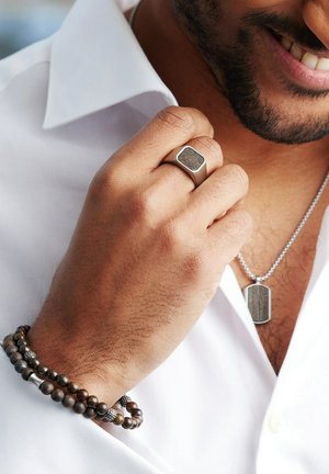 Silver ring with rectangular design, textured dark stone inset. Brown beaded bracelet, silver accents. Silver necklace with engraved pendant.