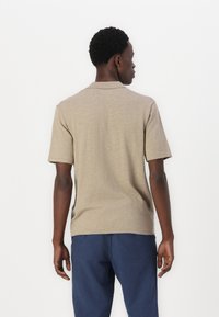 Polo de manga corta beige con tejido texturizado y cuello, combinado con pantalones azul oscuro. Vista desde la espalda, mostrando el ajuste y el estilo.