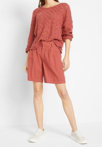 Suéter color óxido con un patrón texturizado de punto abierto, combinado con pantalones cortos de corte holgado a juego. El modelo lleva zapatillas de color claro.