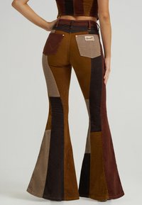Corduroy flared pants featuring a patchwork design in brown, beige, and dark hues. Notable details include accent stitching and back pockets.