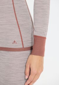 Långärmad topp i ljusgrått med kontrasterande rostfärgade detaljer. Har en strukturerad tyg, figursydd design och en liten logotyp nära fållen.