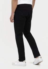 Sorte denim jeans med slim fit, fem lommer og subtile syninger, parret med hvide sneakers, set bagfra.