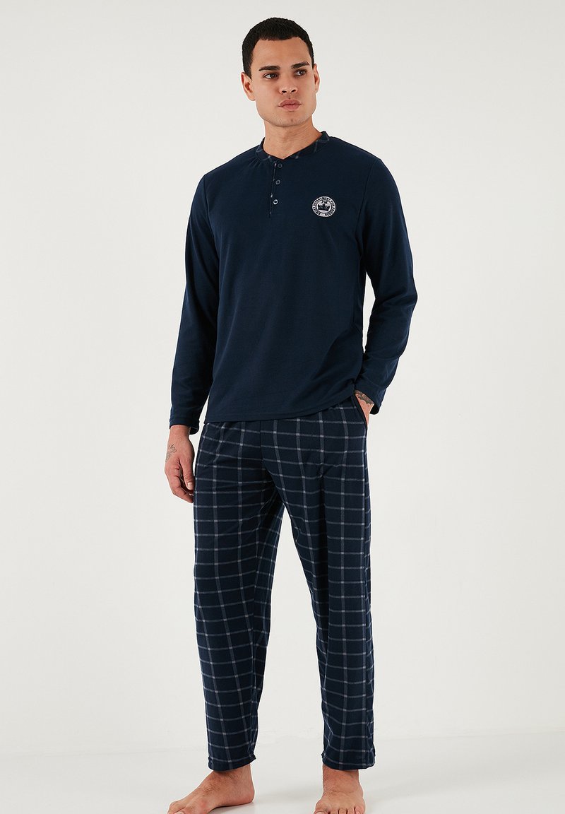 Tricou de pijama cu mânecă lungă de culoare bleumarin, cu decolteu tip henley; pantaloni de pijama asortați cu tartan în nuanțe de albastru închis și alb; material moale și confortabil.