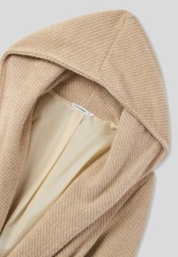 Giacca beige con cappuccio, esterno tessuto e intrecciato con una trama; interno foderato liscio e di colore chiaro. Etichetta interna con la scritta "Terranova".