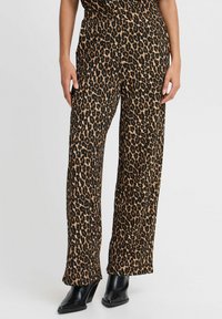 Pantalons larges à imprimé léopard avec une texture douce dans des nuances de marron et de noir, associés à des bottines noires à talons.