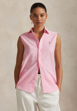 Růžové tílko bez rukávů s rozepínáním na knoflíky a malým vyšitým logem na hrudi. Lehká látka a špičatý límec.