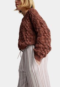 Pull en crochet de couleur rouille, à coupe ample et manches larges. Assorti à un pantalon léger à rayures avec taille à cordon.