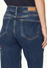 Jeans en denim bleu foncé avec une taille haute, un léger délavage et des coutures contrastées. Deux poches arrière avec une étiquette en cuir de marque à la taille.