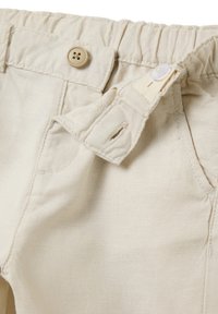 Pantalons en coton beige avec une taille froncée, une fermeture à bouton et une sangle réglable. Comprend une poche avant et une texture douce.