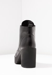 Black leather ankle boot with a chunky heel, smooth finish, and a pull tab at the back. Features a rounded toe and stylish seam detailing.