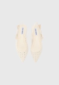 Kengät, joissa on kapea varvas, slingback-malli, vaaleankreemiväristä kangasta, koristeltu hopeisilla niiteillä, ja hienovarainen solmittu yksityiskohta kantapäässä.