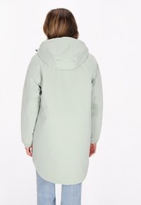 Gaiši zaļš ūdensizturīgs jaka ar kapuci, garām piedurknēm, elastīgiem aprocēm un noapaļotu apakšmalu. Minimalistisks dizains, gluda tekstūra.