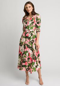 Sukienka w kwiaty z zielonymi, różowymi i białymi wzorami liści. Długie rękawy, ściśnięta talia z kokardą, lekko opadająca do długości midi. Gładki materiał.