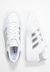 Vita idrottsskor i syntetiskt material, med silverdetaljer, design med tre ränder och en texturerad sula för bra grepp.