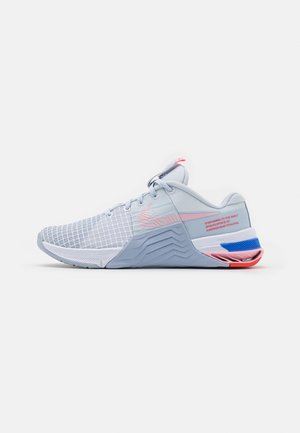 Chaussure de sport gris clair avec des accents roses et bleus, tige en mesh, semelle intermédiaire texturée, et texte sur le panneau du talon sur fond blanc.