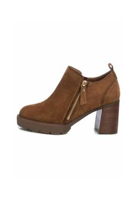 Stivaletti in suede marrone con zip laterale, punta rotonda e tacco in legno impilato. Presentano una tomaia strutturata e una suola in gomma a contrasto.