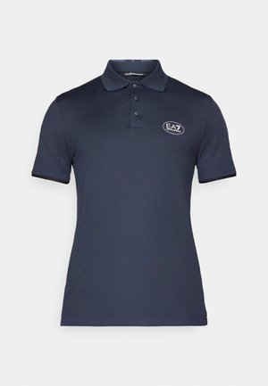 Polo de cor azul-marinho feito de um tecido suave. Apresenta um colarinho pontudo, uma pala com três botões e um logótipo bordado no lado esquerdo do peito.