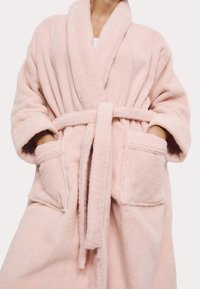 Rosa fluffig badrock med sjalkrage, bälte i midjan och två framfickor. Materialet är mjukt och strukturerat. Halvlånga ärmar.