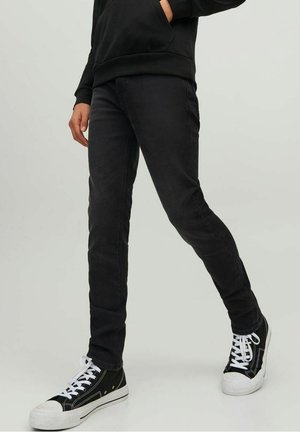 Jean en denim noir à coupe slim, présentant une texture lisse, des coutures minimales et un ourlet roulé, associé à des baskets montantes noires.