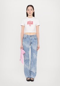 White cropped t-shirt with red "SPACE FOOD" graphic, paired with light blue flared jeans featuring a cloudy pattern. Holding a pink accessory.