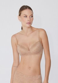 Sostenes de encaje en color nude con escote pronunciado, tirantes ajustables y bordes ondulados. Patrón floral delicado en toda la prenda.