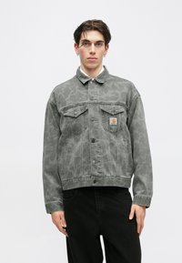 Chaqueta de mezclilla gris con un sutil patrón de estampado animal tonal, cierre frontal de botones, dos bolsillos en el pecho y un parche de marca en el bolsillo izquierdo.