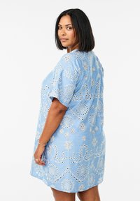 Robe bleu clair avec des motifs de broderie circulaires et des détails en œillets. Manches courtes et coupe décontractée, avec un col rond.