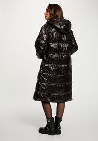 Abrigo acolchado negro con un acabado brillante, que cuenta con capucha, diseño de acolchado horizontal y bolsillos con cremallera. Combinado con botas negras con hebilla.