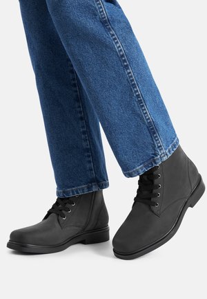 Crne kožne gležnjače s okruglim vrhom, vezicama i glatkim završetkom. Uparene s plavim trapericama ravnog kroja.