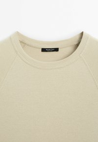 Sweat-shirt beige col rond avec coutures visibles et étiquette de marque noire « Massimo Dutti » cousue à l’intérieur du col.
