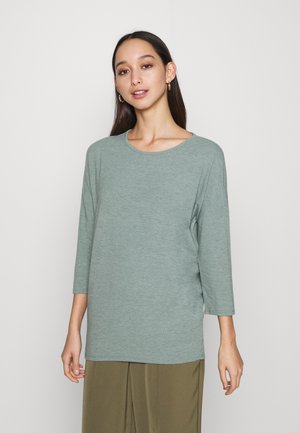 Maglietta a maniche lunghe verde chiaro con scollatura rotonda e vestibilità rilassata. Texture liscia e morbida con un design leggermente drappeggiato.