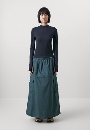 Long-sleeve black top with textured accents paired with a green maxi skirt featuring cargo pockets and an elastic waistband.