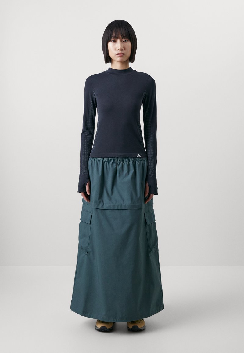 Haut noir à manches longues avec des accents texturés, associé à une jupe maxi verte dotée de poches cargo et d'une taille élastique.